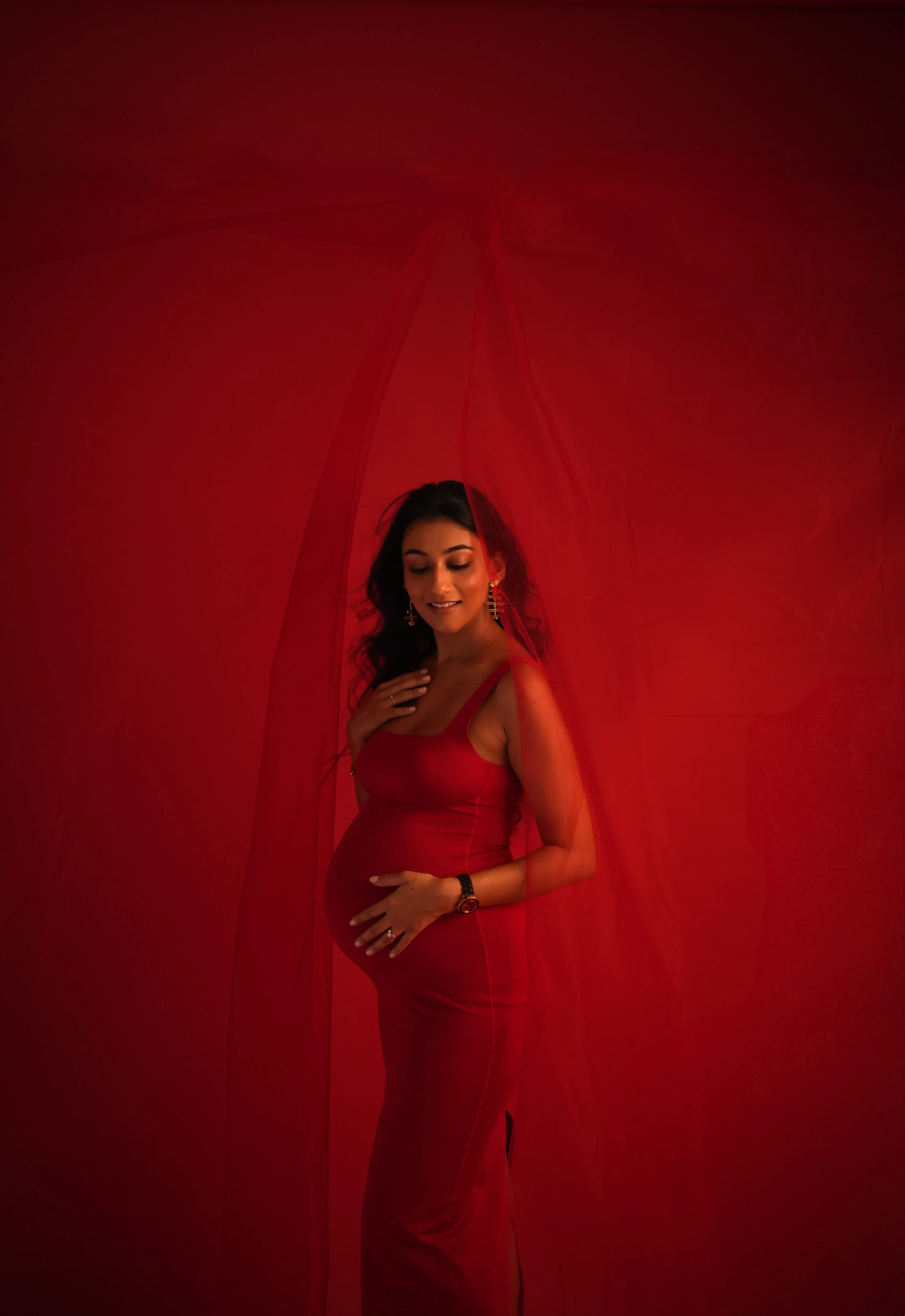 Expecting mother in red dress with soft natural lighting and red background